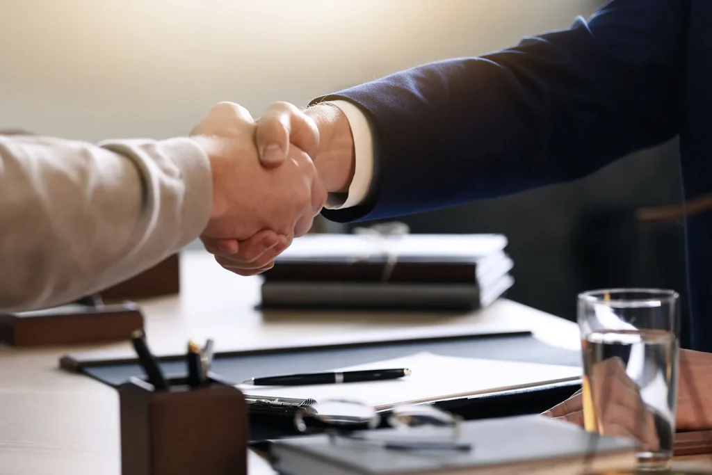 businessmen shaking hands over a desk of paperwork.