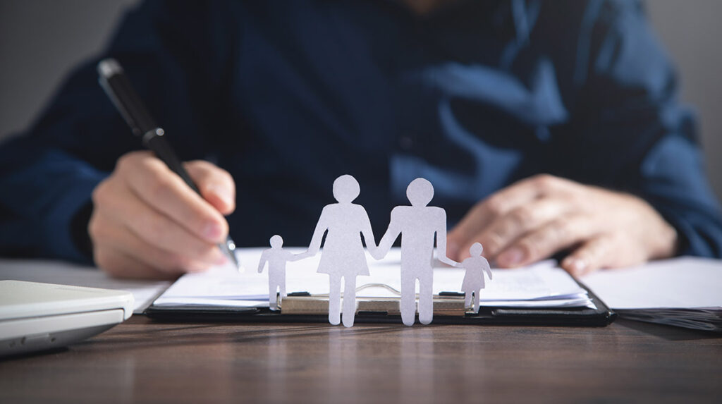 Life Insurance Documents being signed behind a paper cutout of a happy family.
